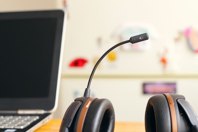A headset with a microphone beside a laptop on a desk