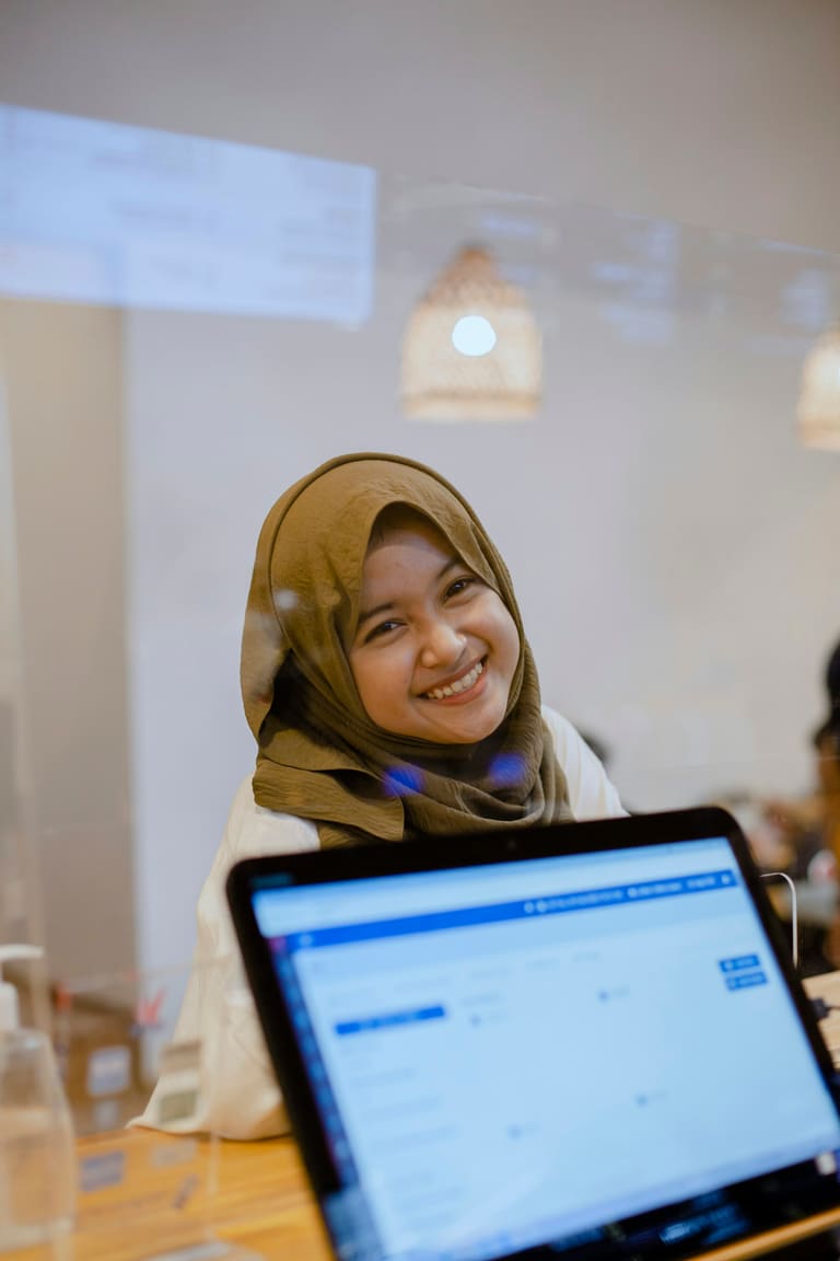 A smiling service representative in a headscarf at a laptop